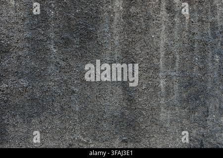 Close up view of a dark, heavily weathered concrete wall with a very rough surface. An industrial grunge texture ideal for abstract dark backgrounds. Stock Photo