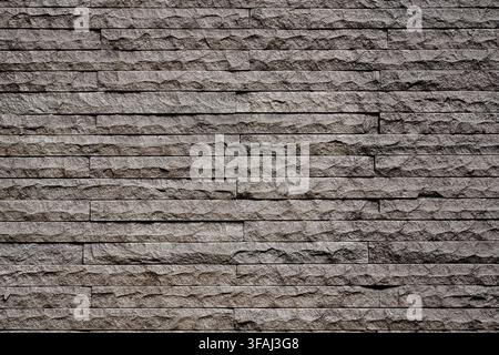 Close up of a dark grey textured stacked stone wall. A modern natural stone veneer cladding surface ideal for architectural and interior design. Stock Photo
