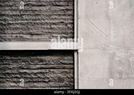 Abstract architectural background featuring a contrast between dark rough stacked stone veneer and smooth light grey concrete panels. Stock Photo