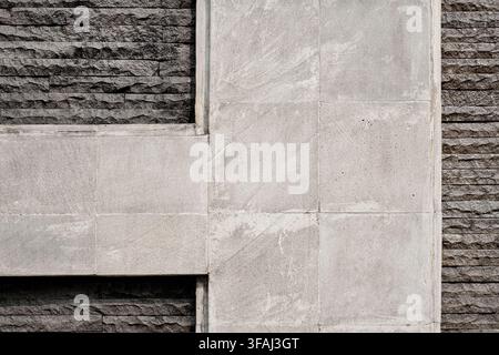 Modern architectural wall texture featuring interlocking light grey concrete panels and rough dark grey stacked stone veneer. Stock Photo