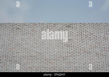 A solid white painted brick wall against a clear light blue sky. Minimalist architectural background with clean lines and ample copy space. Stock Photo
