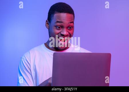 Closeup Shot Of Excited Black Guy Using Laptop Computer Under Neon Lighting Stock Photo