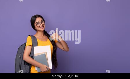 Smiling indian student wearing eyeglasses holding notebooks showing thumbs up Stock Photo