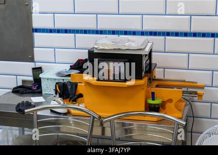 Edible ink printer with visible cartridges sits on yellow stand over stainless steel counter in kitchen room with white tiled wall, gloves, basket, an Stock Photo