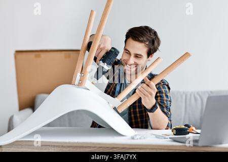 Man fixing furniture, repairing wooden chair, using electric drill at home Stock Photo