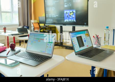 Laptops Displaying Coding Software on Desks in Empty Classroom Stock Photo