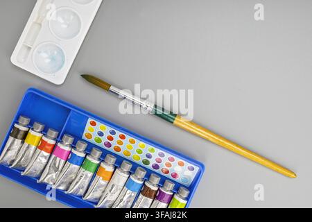 Watercolor paint tubes in a blue plastic tray with an artist paintbrush and mixing palette resting on a sleek grey background with open copy space. Stock Photo