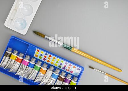 Overhead view of watercolor paints in tubes with wooden brushes and palette on a smooth gray background ready for art and creative painting tasks. Stock Photo