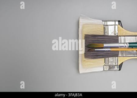 Stack of different artist paintbrushes and flat decorating brushes arranged on a minimal grey tabletop with clear negative space for artwork copy. Stock Photo