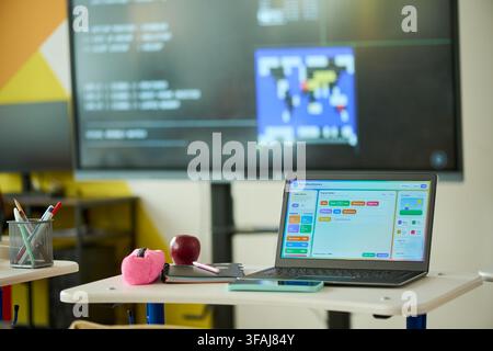 Laptop Displaying Coding Software on Desk in Modern Classroom Stock Photo