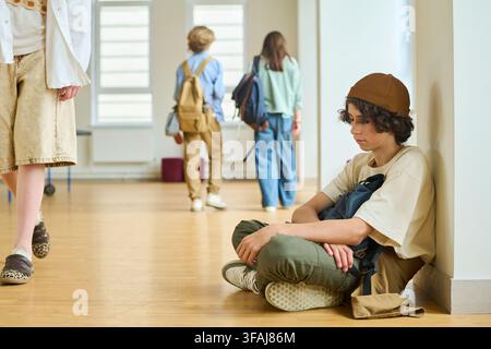 Sad Teenager Sitting Alone on Floor in School Corridor Stock Photo