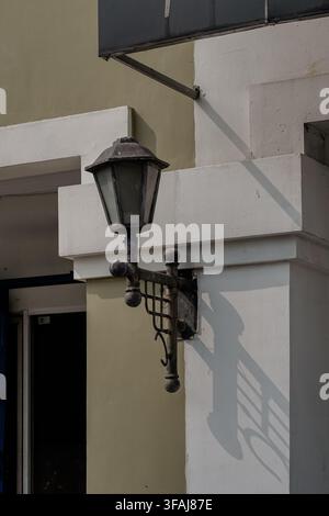 Close-up detail shot of a classic black iron lantern light fixture mounted on a light grey wall column, casting a dark geometric shadow. Stock Photo