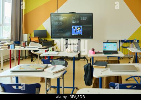 Empty Modern Classroom Displaying Coding Lesson on Interactive Screen Stock Photo