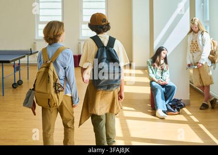 Teenagers with Backpacks Walking in School Hallway during Break Stock Photo