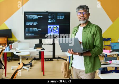 Portrait of Indian Middle Aged IT Teacher Holding Laptop in Classroom Stock Photo