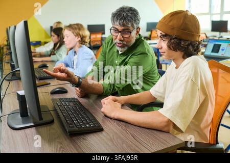 South Asian Teacher Helping Teenager Boy with Computer Coding in Classroom Stock Photo