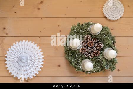 Top view of a handmade Advent wreath decorated with evergreen branches pinecones and four white candles arranged on a natural wooden tabletop. Stock Photo