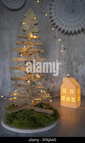 Elegant Christmas still life featuring a modern wooden Christmas tree with warm fairy lights and an illuminated decorative house creating a cozy festi Stock Photo