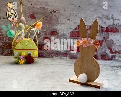 Charming Easter decoration featuring a wooden bunny holding a colorful basket displayed in front of a rustic brick wall with spring accents. Stock Photo
