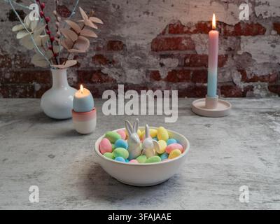 Elegant Easter still life featuring pastel decorative eggs in a bowl with candles and a spring floral arrangement creating a soft seasonal atmosphere. Stock Photo