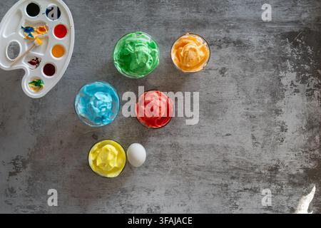 Creative Easter composition featuring colorful marbled eggs in glass bowls alongside watercolor paints and brushes arranged in a bright spring flat la Stock Photo