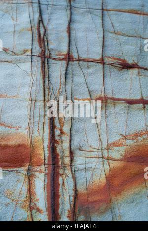 Abstract rock surface with iron oxide grid patterns and blue mineral inclusions. Stock Photo