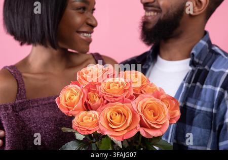 Pair of sweethearts holding beautiful bouquet of roses for Valentine's Day over pink studio background, selective focus Stock Photo