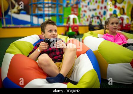 Children holding controllers and playing video games in bean bag chairs Stock Photo