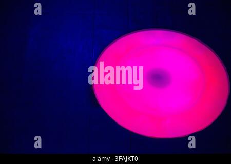 An abstract photograph of a glowing pink and magenta circular light installation contrasted against a dark blue background at a night attraction Stock Photo