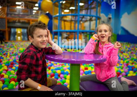 Two children sitting at a purple table in a ball pit Stock Photo