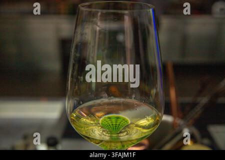 A macro close-up shot of a clear wine glass half-filled with chilled white wine, showcasing a creative patterned distortion inside the liquid against Stock Photo