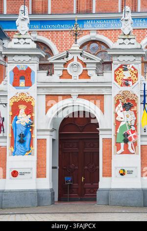 Ornate civic entrance presents a tall wooden door between painted figures and elaborate brick details on the House of the Blackheads in Riga for archi Stock Photo