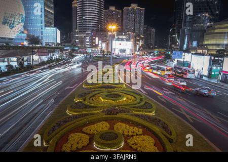 Aerial view of the Xujiahui district at night, featuring busy traffic with light trails on the road, illuminated skyscrapers, and a decorative landsca Stock Photo