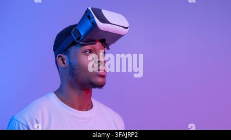 Handsome Black Man Wearing VR Glasses Looking Aside Over Purple Background Stock Photo