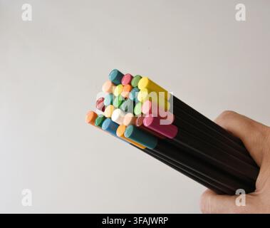 A hand holding several colorful pencils on a clean white table, showcasing creativity, vibrant colors, vintage stationery, and a simple artistic compo Stock Photo