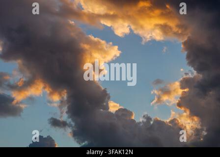 Beautiful golden hour sunlight illuminating dramatic storm clouds with a bright clear blue sky visible through an opening. Hope and optimism concept. Stock Photo