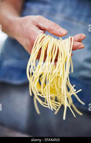 Homemade noodles in hand. The process of making fresh pasta from scratch. A hand covered in flour, holding freshly made noodles, with a blue apron vis Stock Photo
