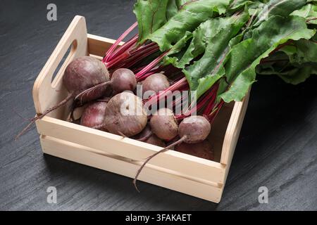 Many young beets with green leaves in wooden crate on dark textured table, closeup Stock Photo