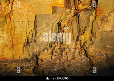 Warm golden rock wall with layered mineral formations and natural cracks. Dramatic geological texture suitable for abstract backgrounds. Stock Photo