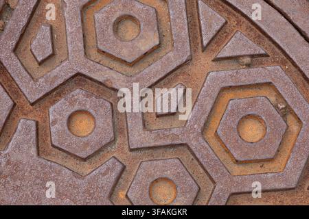 Close-up of a weathered rusty metal surface with a repeating raised geometric pattern and worn industrial texture. Stock Photo