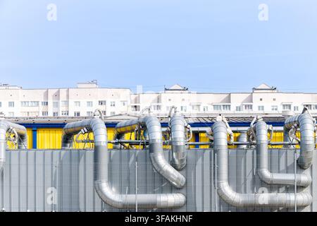 Industrial ventilation system with large metal air ducts and pipes on a factory building against residential blocks and clear blue sky. Stock Photo