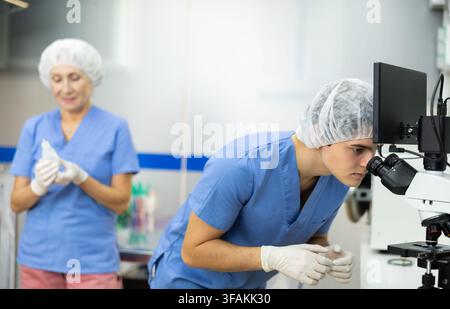 Young veterinarian using microscope to examine blood samples of animal patient Stock Photo