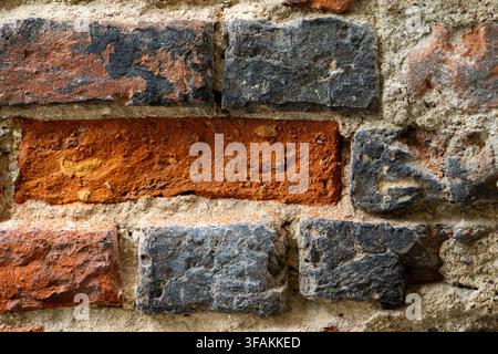 A weathered brick wall features irregular masonry with mixed gray and brown tones. Rough surfaces and varied mortar lines. Stock Photo