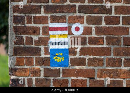 Trail markers appear on a brick wall with colorful stripes and a stylized shell symbol often used on pilgrimage routes. Stock Photo