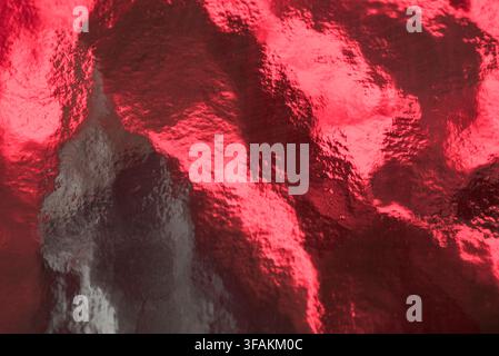 Vibrant red textured glass surface with a dramatic glowing abstract pattern. Stock Photo