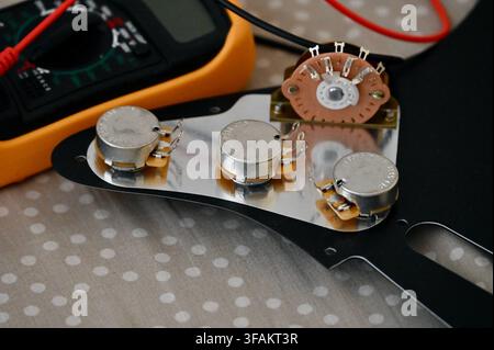A commercial close-up photograph of an electric guitar circuit repair, showing guitar electronics mounted on a pickguard alongside a digital multimeter with red and black test probes. The setup highlights the technical troubleshooting and maintenance of musical instruments. Stock Photo