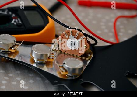 A commercial close-up photograph of an electric guitar circuit repair, showing guitar electronics mounted on a pickguard alongside a digital multimeter with red and black test probes. The setup highlights the technical troubleshooting and maintenance of musical instruments. Stock Photo