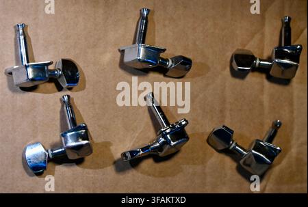 A commercial top-down photograph of a complete set of six shiny chrome electric guitar tuning pegs (machine heads) arranged neatly on a textured brown surface. The polished metal finish and mechanical gear details are clearly visible, highlighting musical instrument hardware and parts. Stock Photo