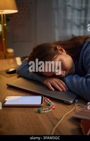 Vertical of Exhausted Woman Sleeping on Closed Laptop at Desk Stock Photo