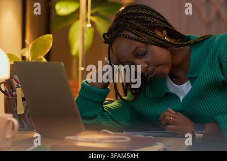 Tired Black Woman Working Late on Laptop in Home Office Stock Photo